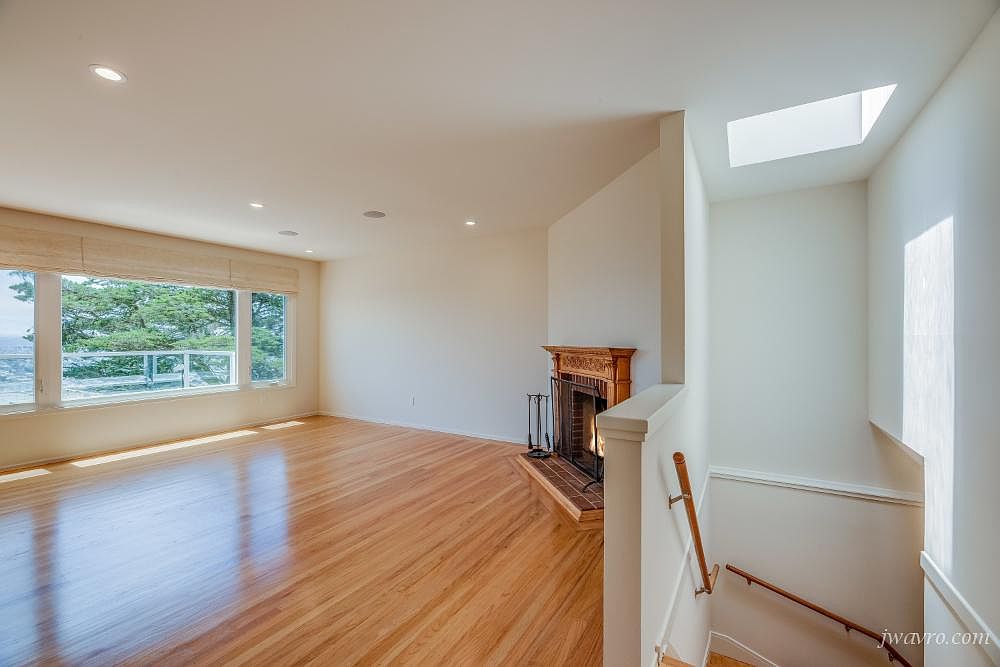 Living room with a wide window looking out to treetops and a brick fireplace