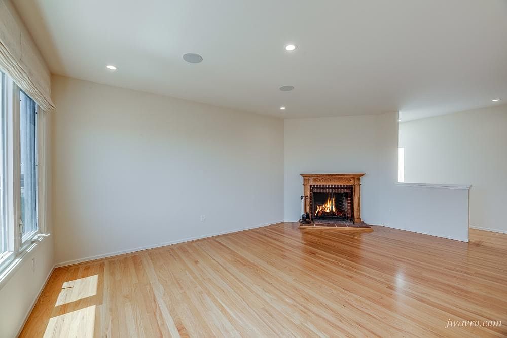 Empty living room with a lit fireplace and hardwood floors