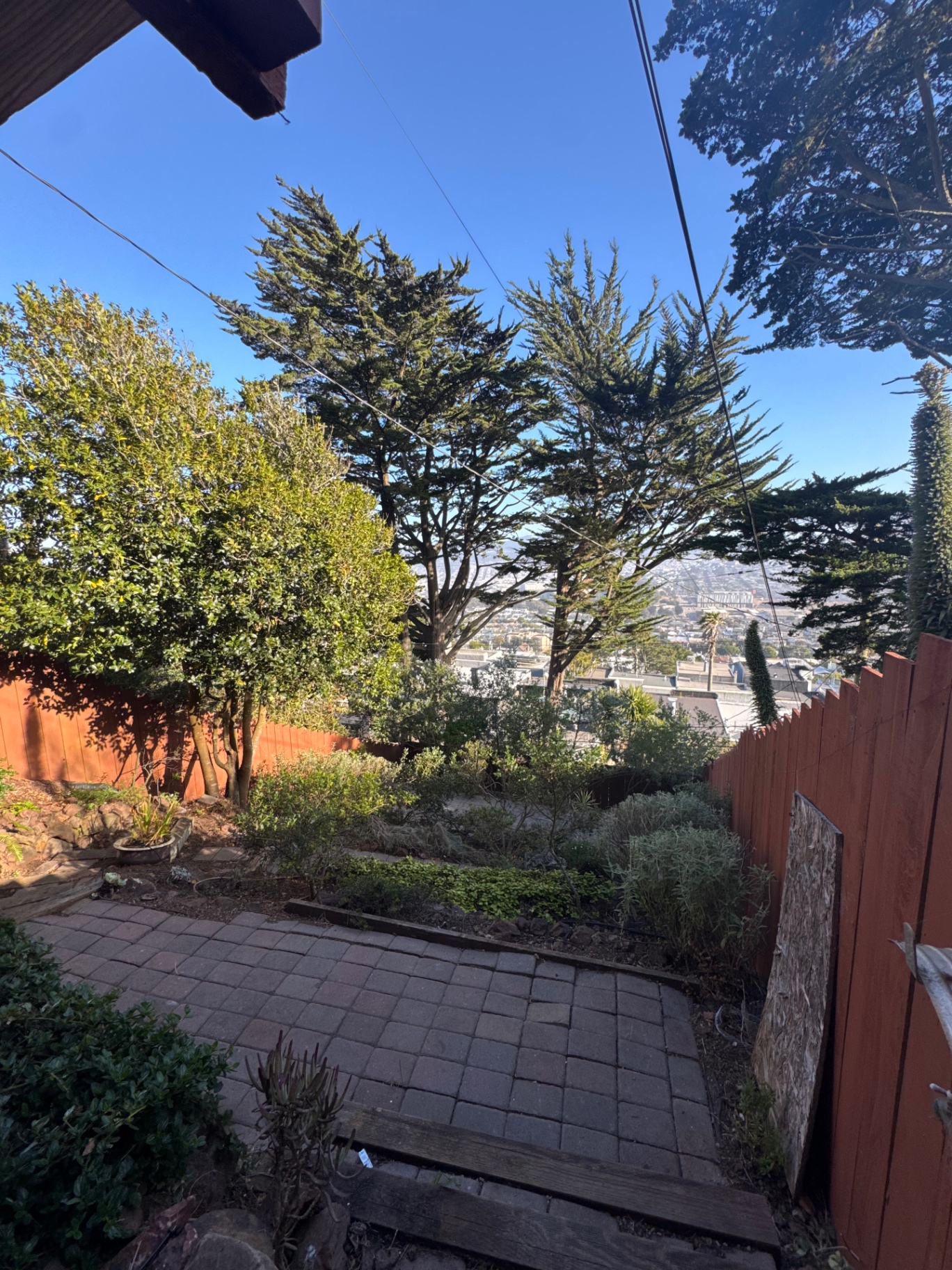Back garden with paver patio, planted beds, and a view over the city
